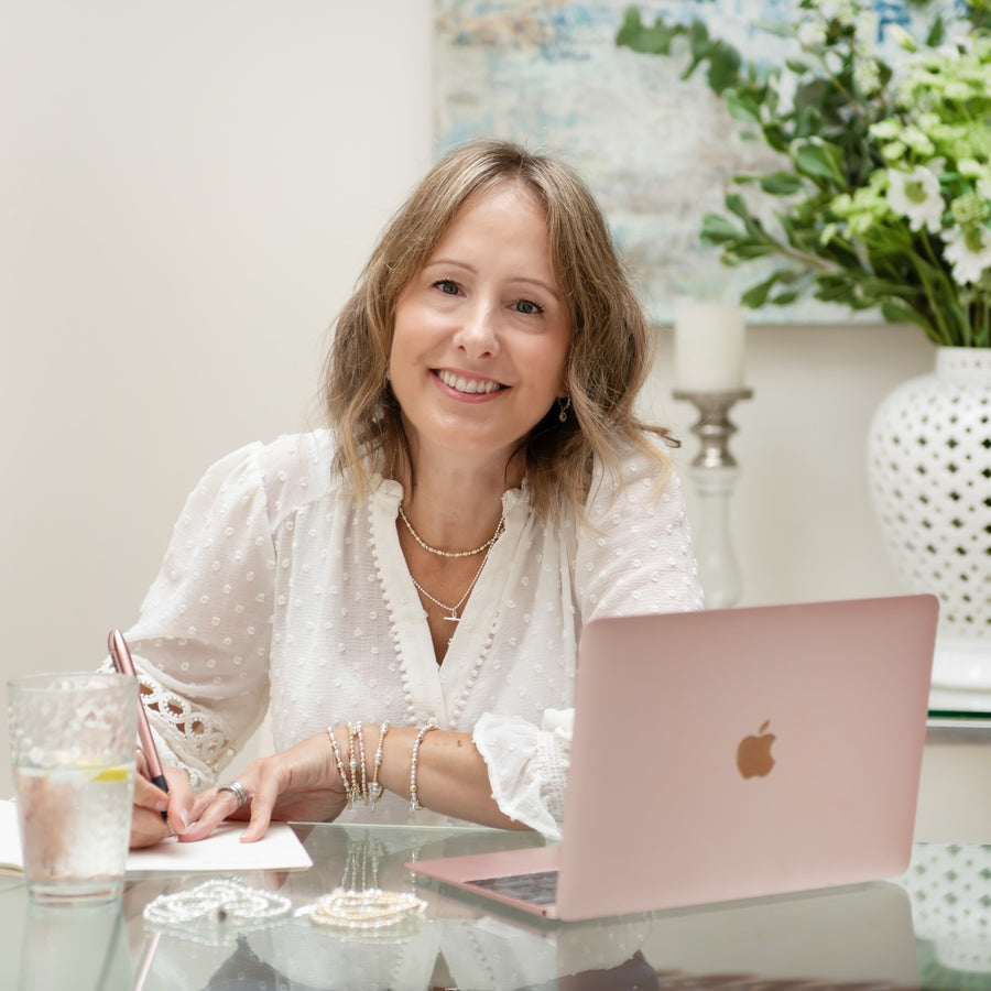 A close up of Bella Jane founder, Annabel sitting at a desk with a laptop with flowers in the background