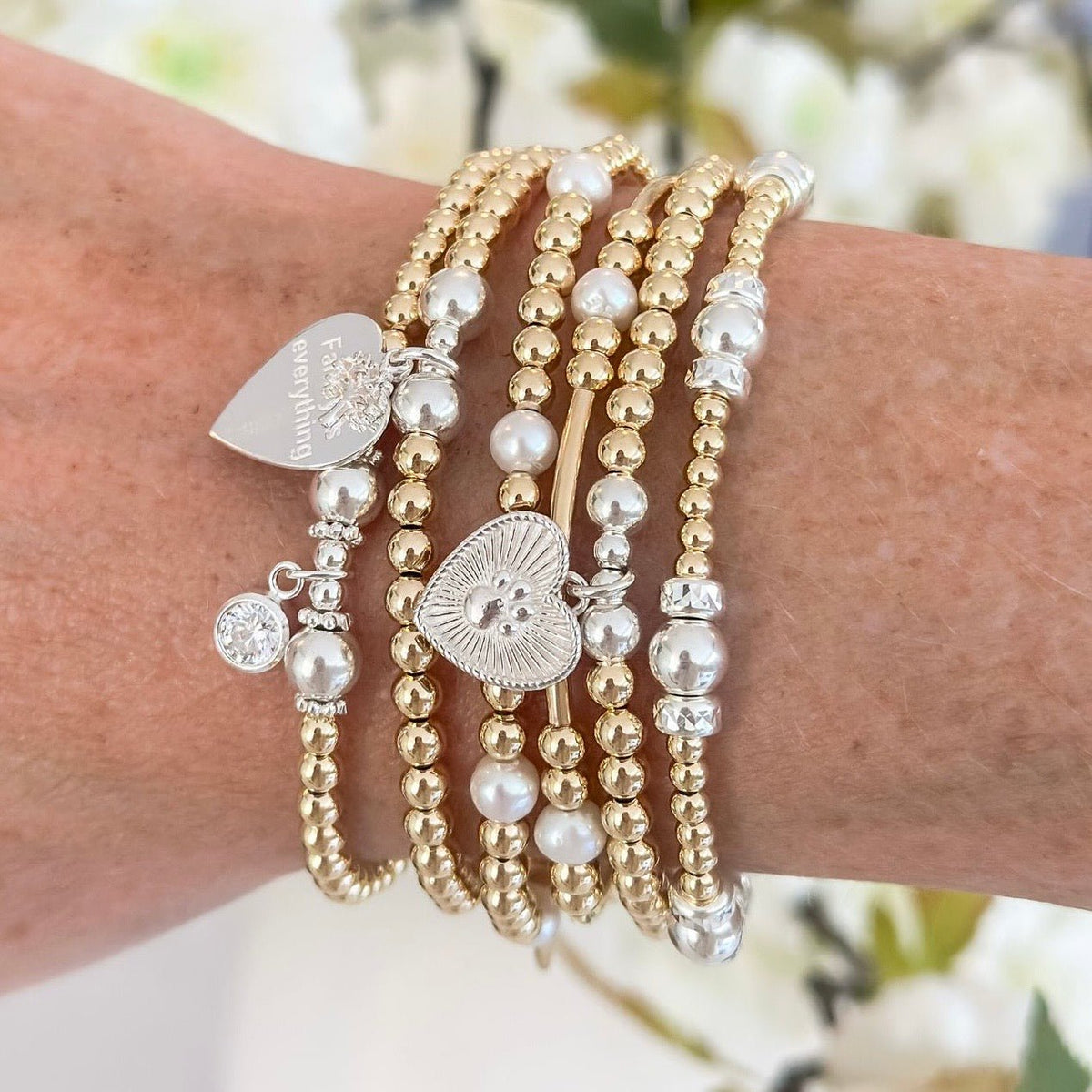 Stack of gold and pearl beaded bracelets on a wrist with a blurred floral background