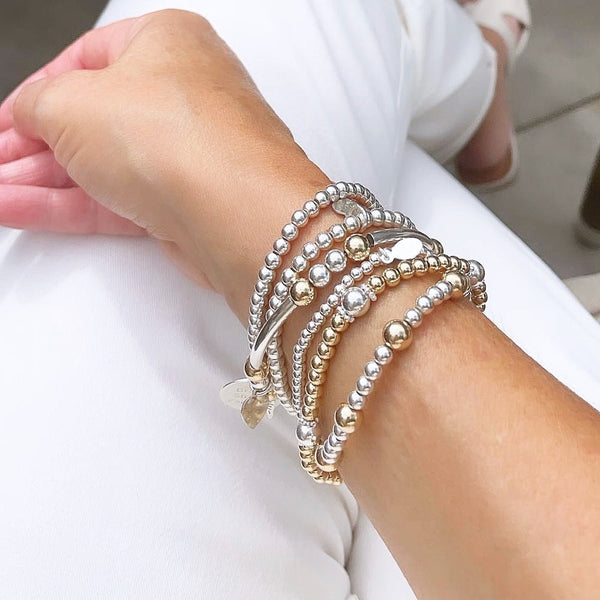 Stack of silver and gold beaded bracelets on a wrist against a white background