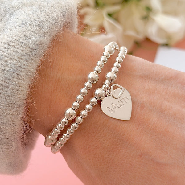 Two silver beaded bracelets on a wrist with a heart-shaped 'Mum' charm.
