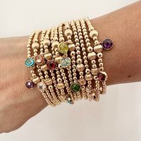 A close-up wrist shot of a woman's wrist wearing a stack of gold birthstone bracelets, with different coloured cubic zirconia birthstone charms.
