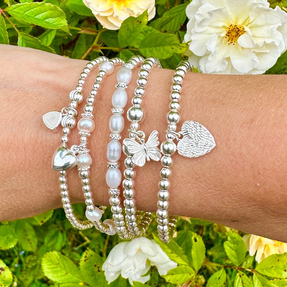 Silver bracelets with heart and butterfly charms on a wrist against a floral background