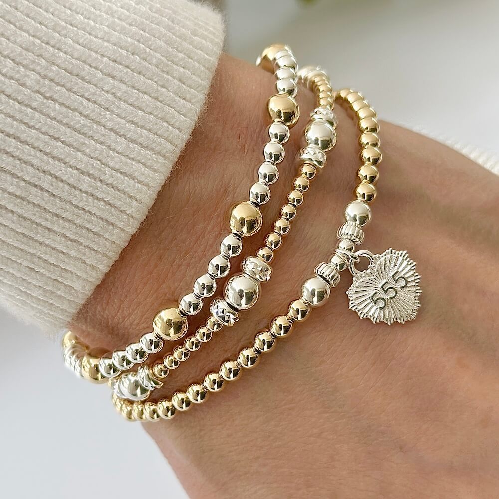 A close-up photo on a white background, of a gold-filled beaded bracelet with sterling silver focal beads and silver heart-shaped charm, featuring angel number 555 on the front of the charm.