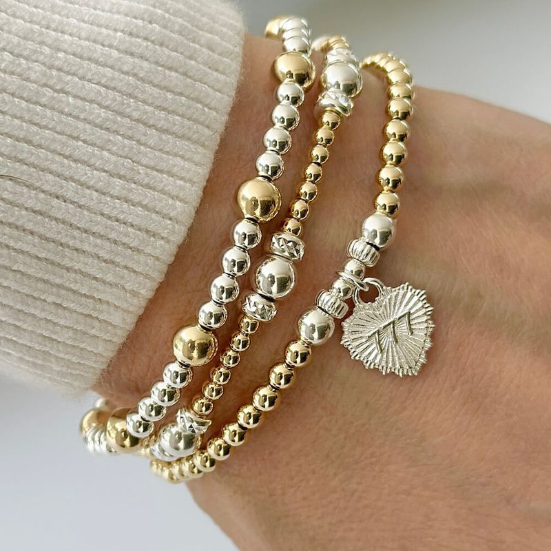 A close-up photo on a white background, of a gold-filled beaded bracelet with sterling silver focal beads and silver heart-shaped charm, featuring angel number 777 on the front of the charm.