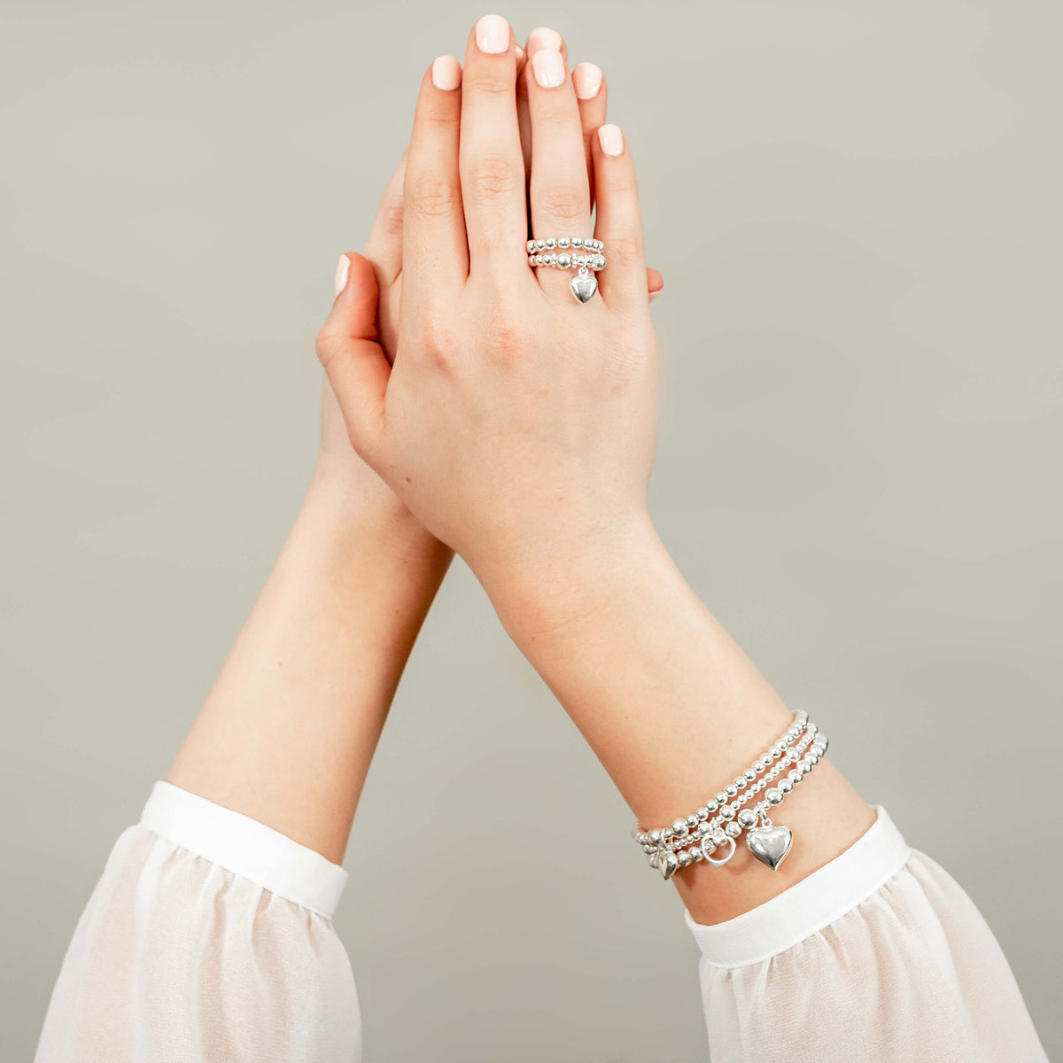 Close-up of hands wearing silver rings and bracelets on a neutral background