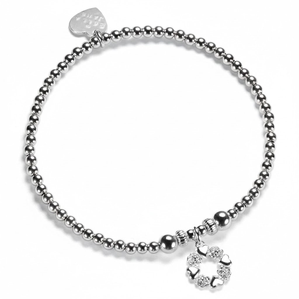 A Bella Jane silver beaded bracelet on a white background, featuring a silver wreath-shaped charm with alternate little hearts and roses
