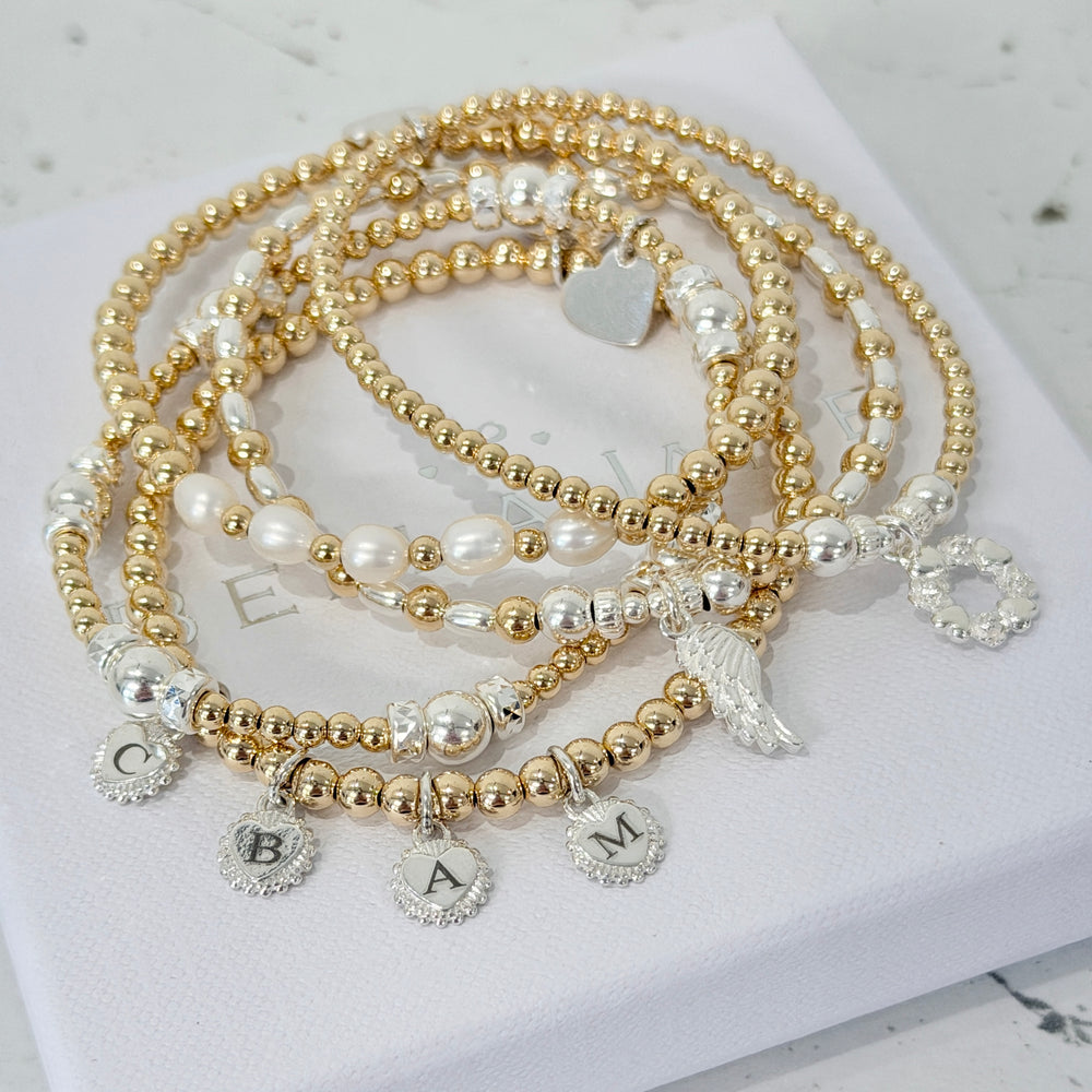 Anna Corry's curated bracelet stack, featuring a set of five gold-filled, sterling silver and pearl beaded bracelets with charms, laid on a white surface