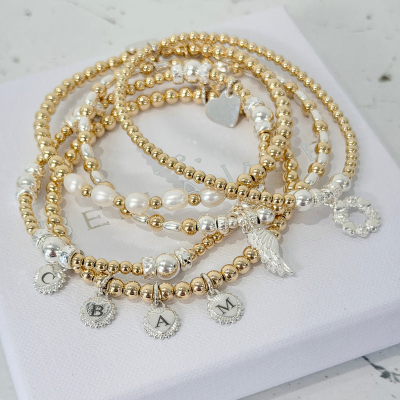 Anna Corry's curated bracelet stack, featuring a set of five gold-filled, sterling silver and pearl beaded bracelets with charms, laid on a white surface