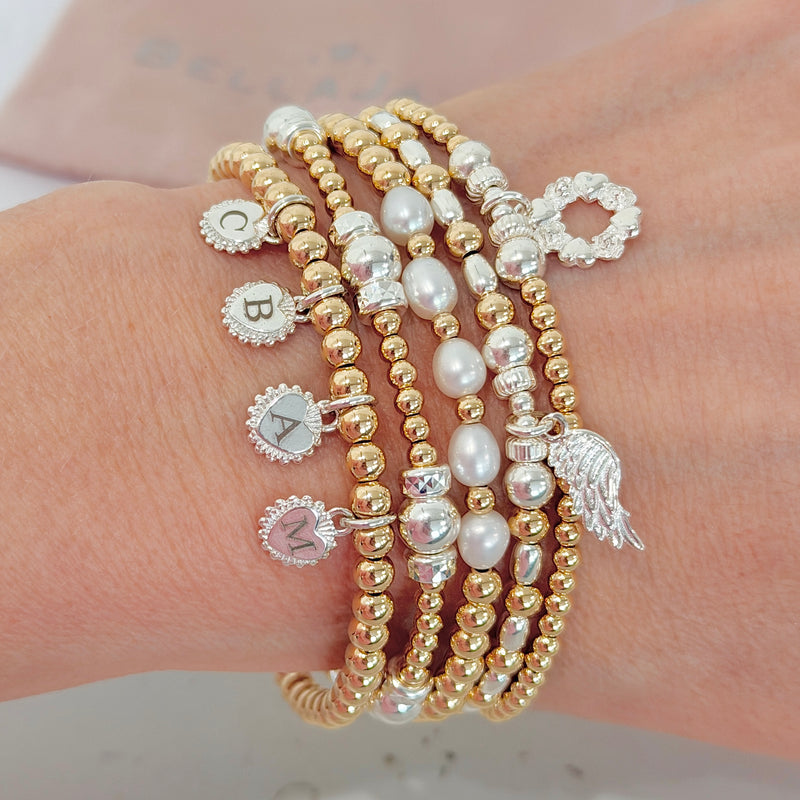 A close up wrist shot of the Anna Corry (Instagram's blossomingbirds) Bella Jane stacking bracelet edit, featuring five gold, silver and pearl beads, with charms against a neutral background