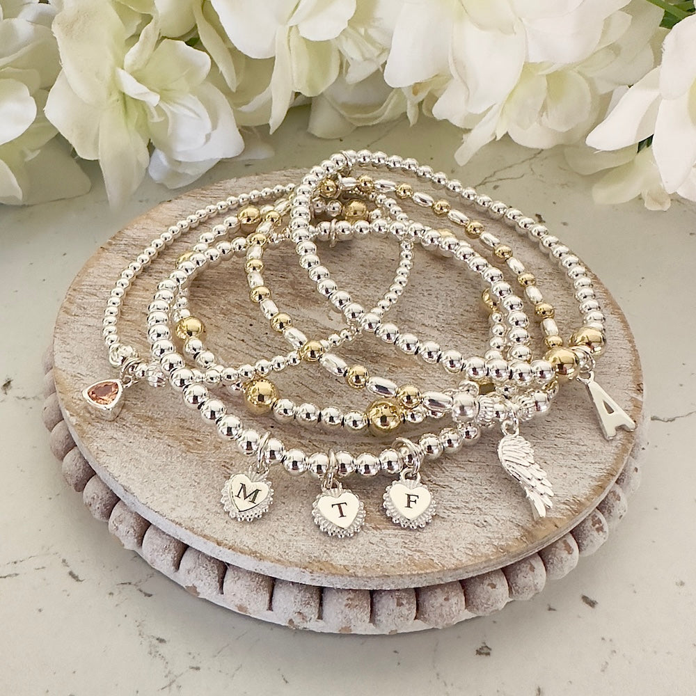Set of beaded bracelets with charms on a wooden stand with flowers in the background