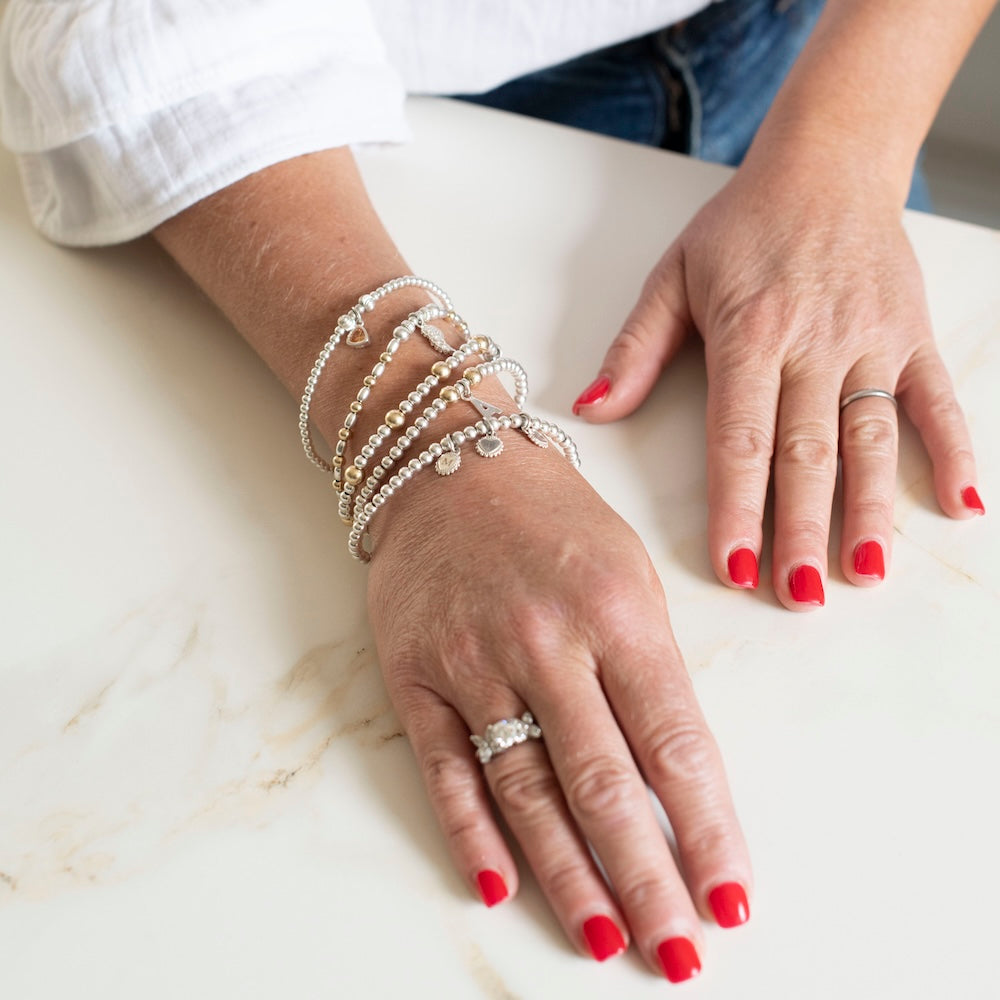 Close-up of hands wearing multiple silver bracelets on a light surface