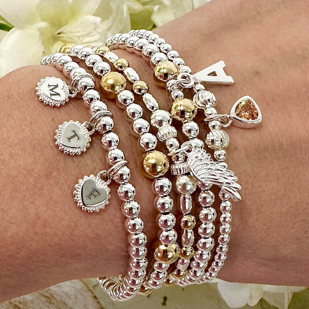 Multiple Bella Jane sterling silver and gold-filled stacking bracelets with charms on a wrist against a floral background