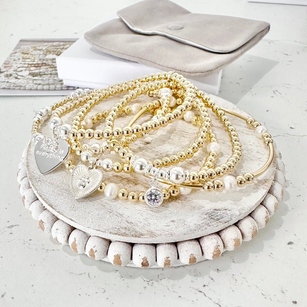 Set of gold, silver and pearl beaded bracelets on a wooden stand with a white background