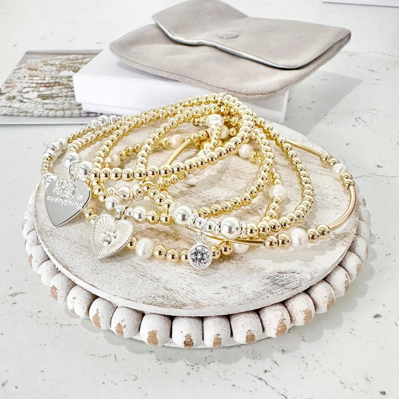 Set of gold, silver and pearl beaded bracelets on a wooden stand with a white background