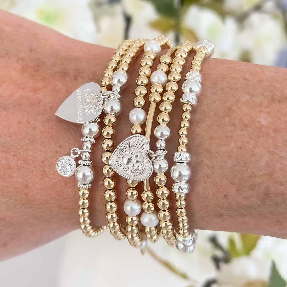 Close-up of a wrist wearing multiple gold, silver and pearl beaded bracelets with charms.