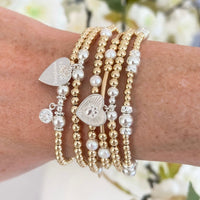 Close-up of a wrist wearing multiple gold, silver and pearl beaded bracelets with charms.