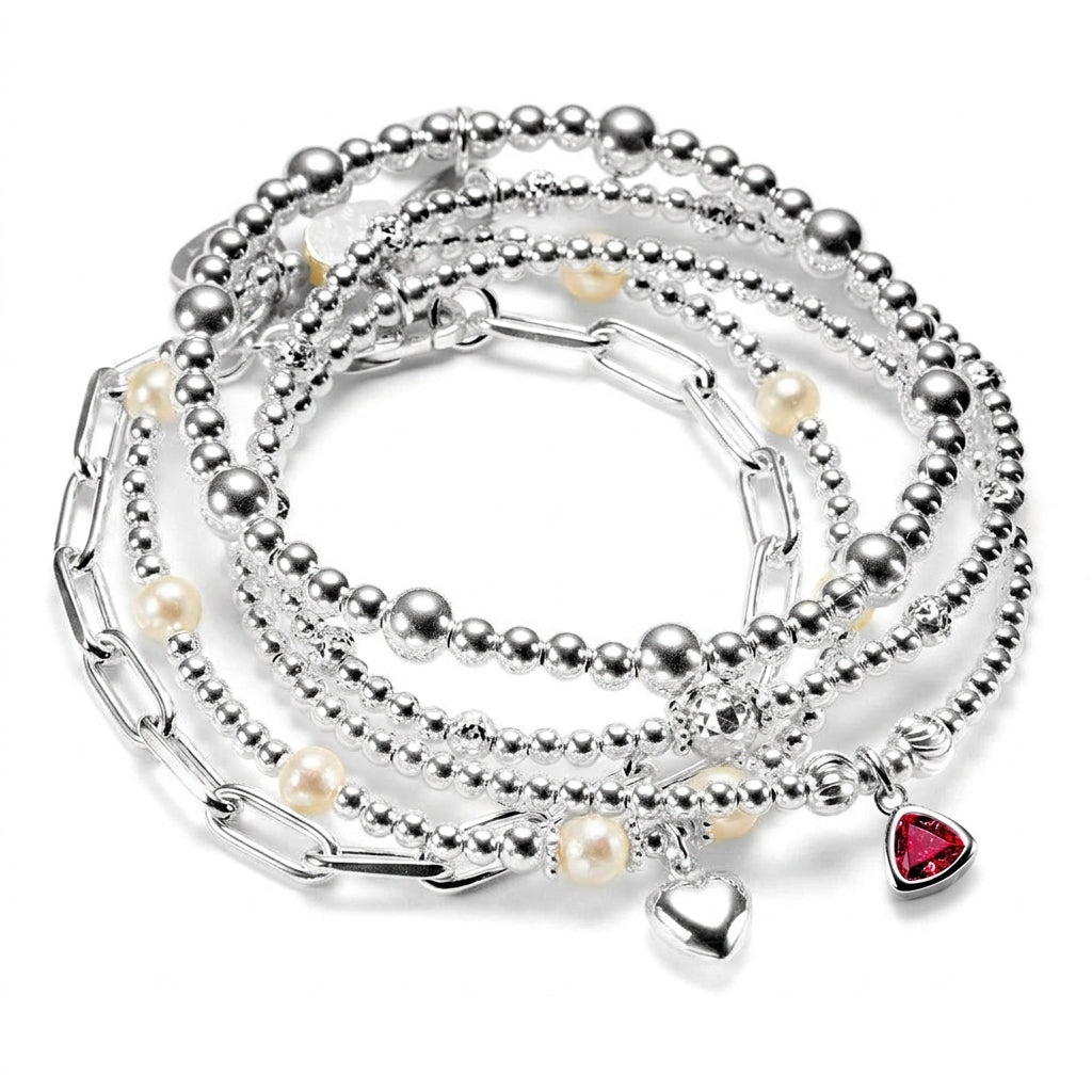 The Bestsellers Stack of sterling silver bracelets with pearls, a heart charm and a garnet-coloured January birthstone charm, on a white background