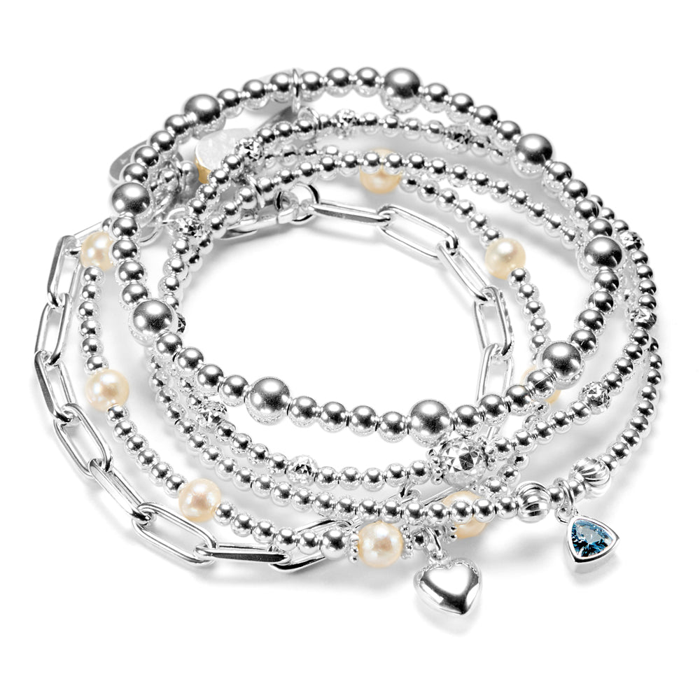 Stack of silver beaded bracelets with pearls, heart charm, birthstone charm, on a white background
