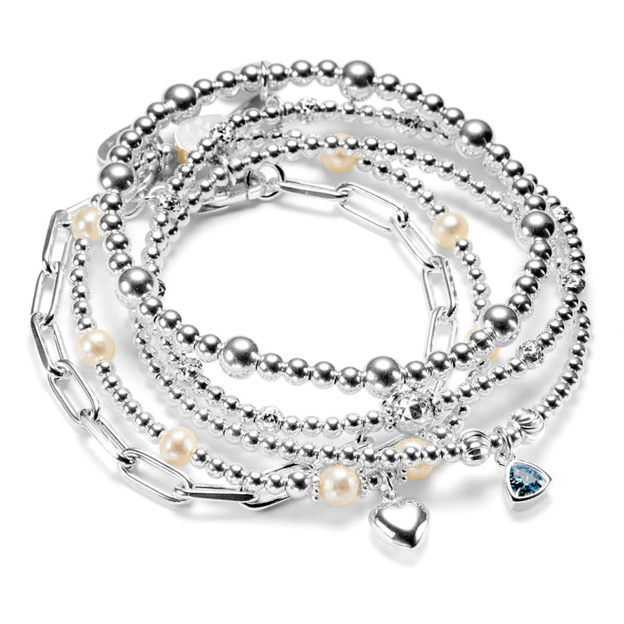 Stack of silver beaded bracelets with pearls, heart charm, birthstone charm, on a white background