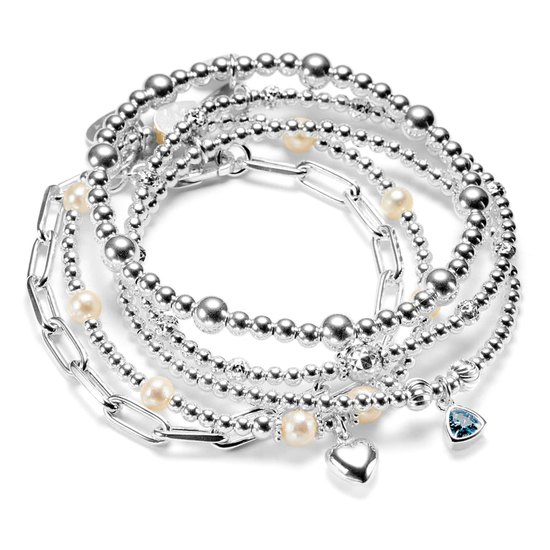 Stack of silver beaded bracelets with pearls, heart charm, birthstone charm, on a white background