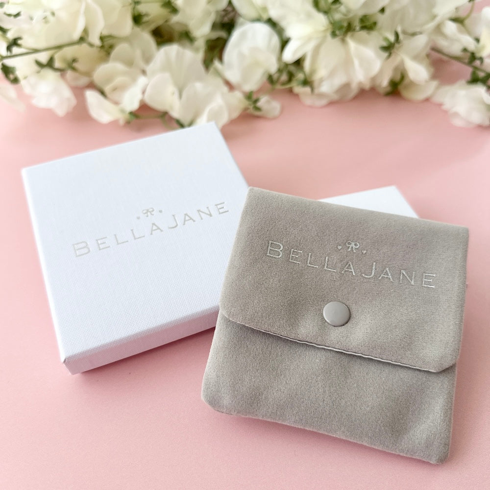 Grey velvet pouch and white box with 'Bella Jane' branding on a pink background with white flowers.