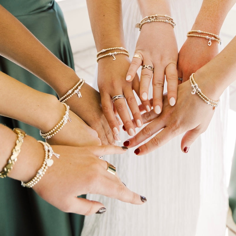 A close up of 7 hands all wearing beaded stacking bracelets