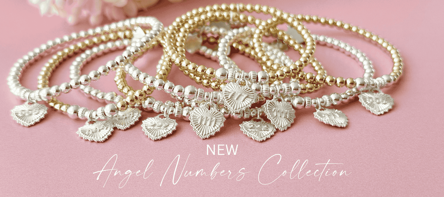 A set of stacking bracelets with heart charms with angel numbers on a pink background, labeled 'NEW Angel Numbers Collection'.