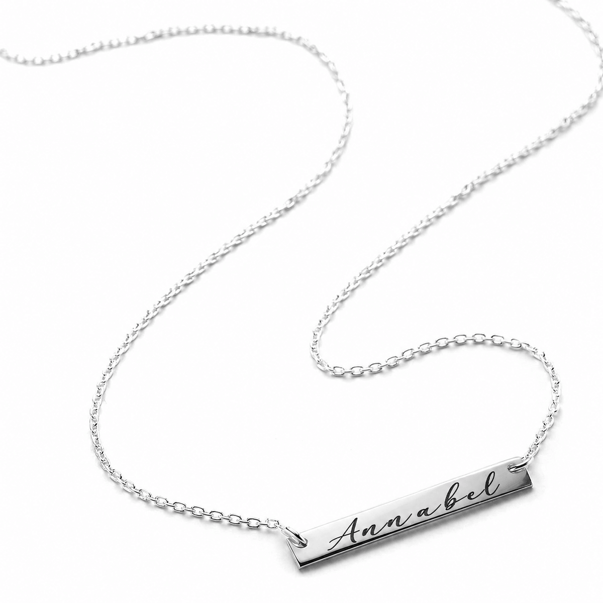 A silver nameplate necklace with a delicate cable chain, featuring a rectangular bar engraved with the name 'Annabel' in cursive, shown on a clean white background.
