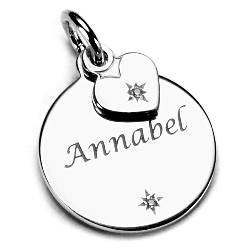 Close up of a round disc charm with a small hearing attached and tiny sparkle, with the name 'Annabel' engraved on the charm