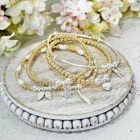 Set of gold and silver beaded bracelets on a wooden surface with flowers in the background