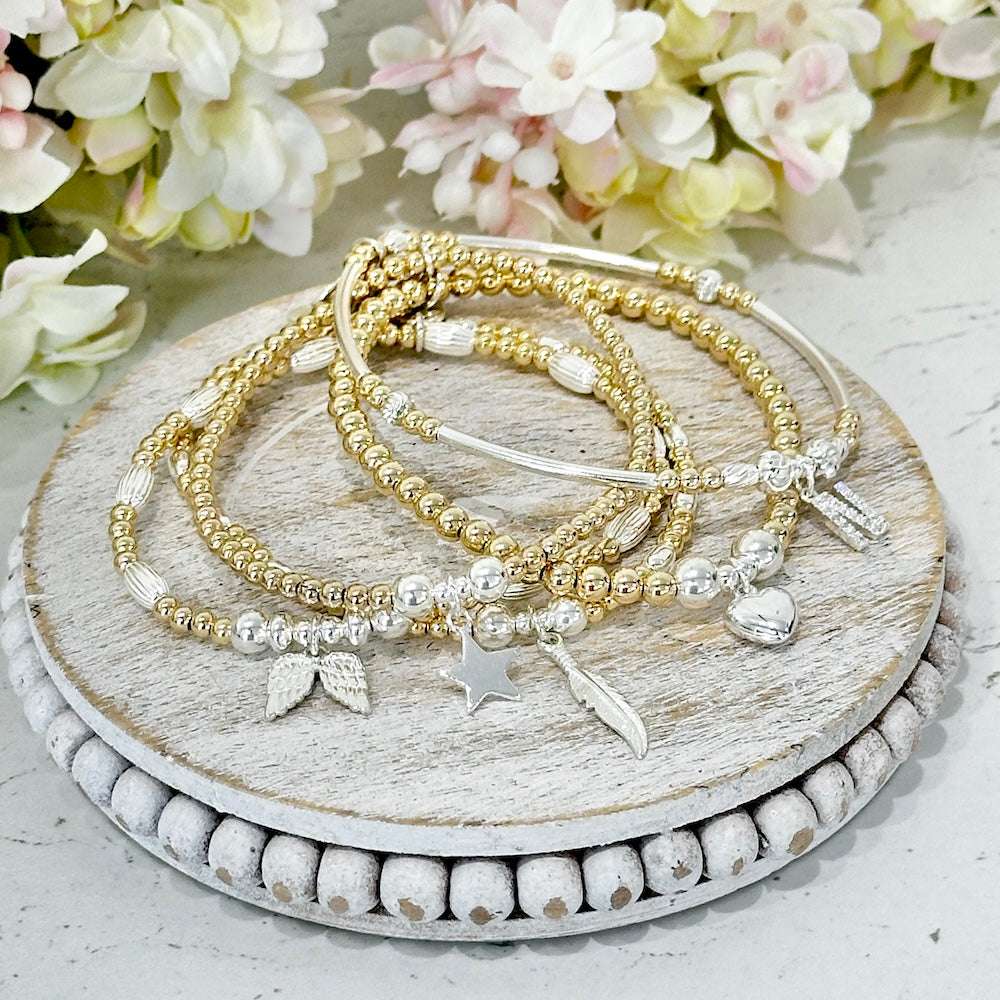 Set of gold and silver beaded bracelets on a wooden surface with flowers in the background