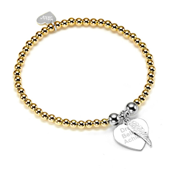 A gold stacking bracelet with a silver heart-shaped charm engraved with 'Dream believe achieve' on a white background