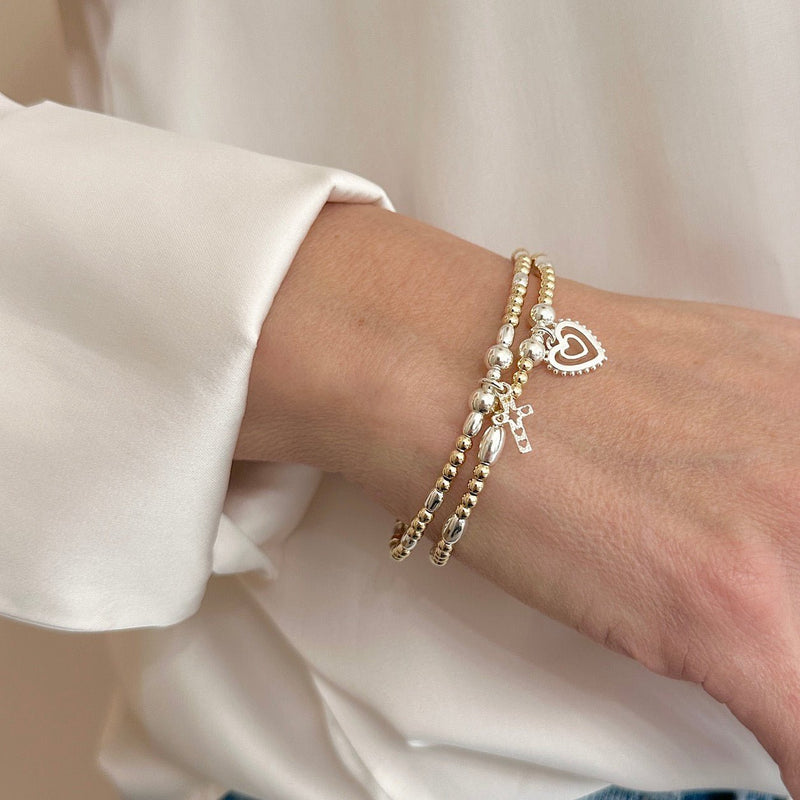 2 Gold and silver stacking bracelets with heart and cross charm on a wrist against a neutral background