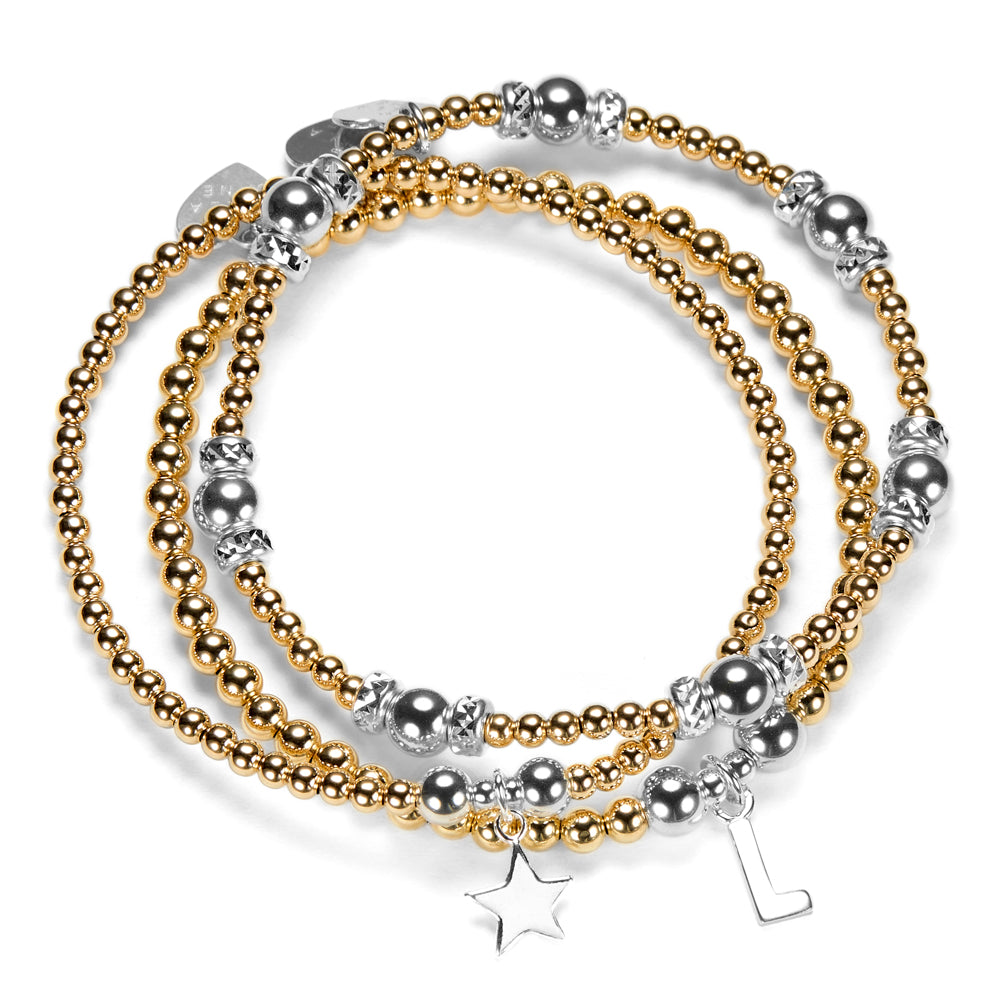 Stack of silver and gold mixed metal beaded bracelets with star and initial charms on a white background