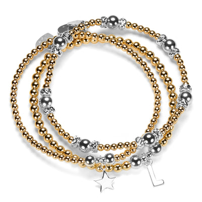 Stack of silver and gold mixed metal beaded bracelets with star and initial charms on a white background