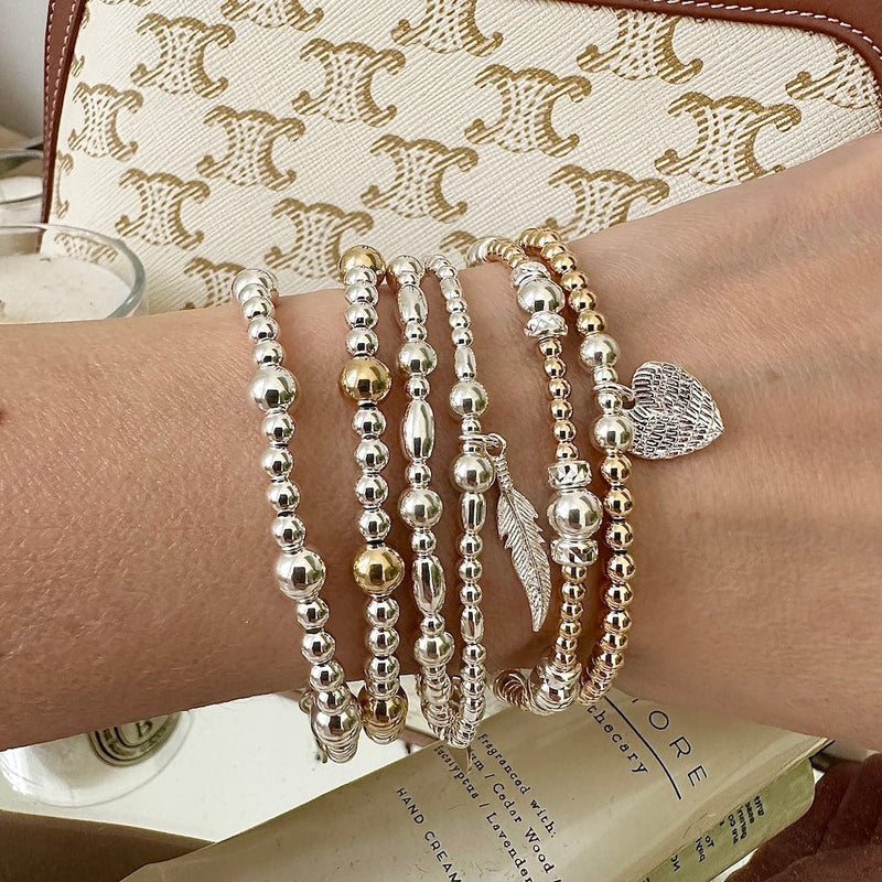 Silver and gold beaded bracelets on a wrist with a patterned background