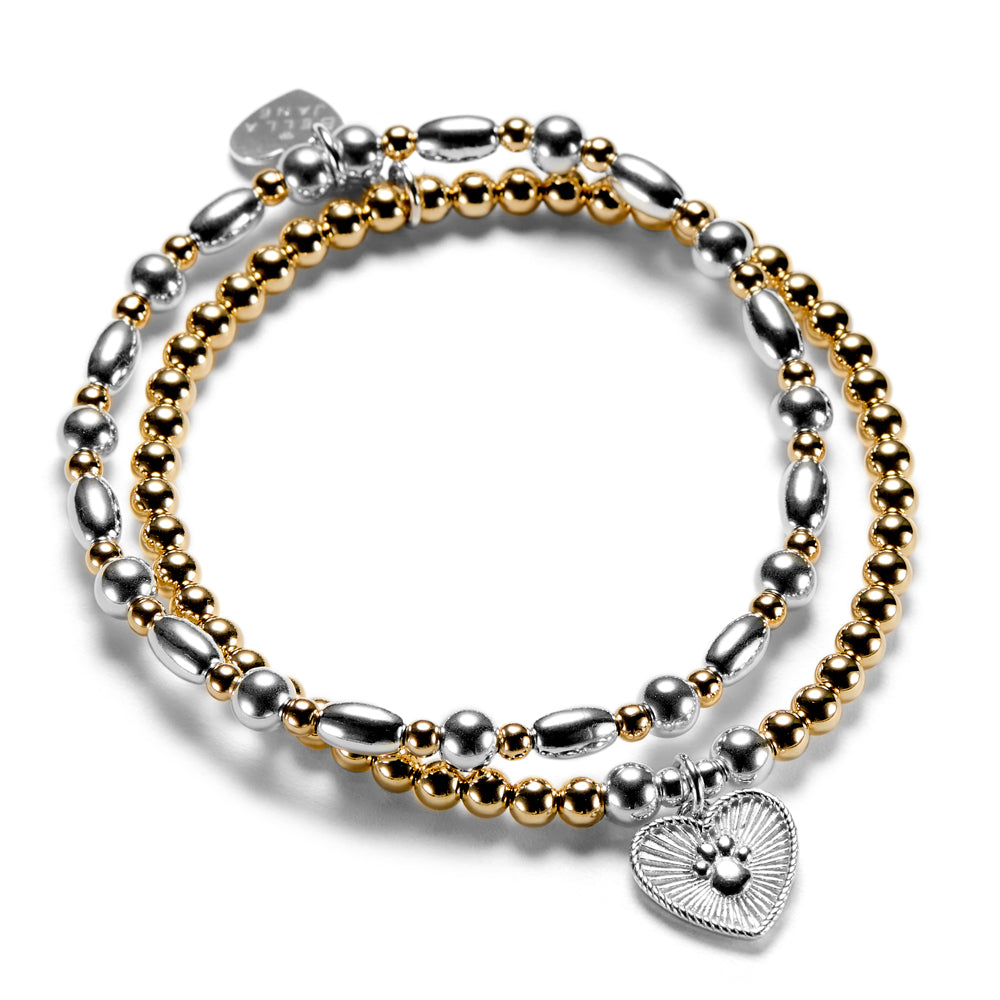 A gold and silver mixed metal beaded stacking bracelet duo with one bracelet featuring a silver paw print heart charm, on a white background