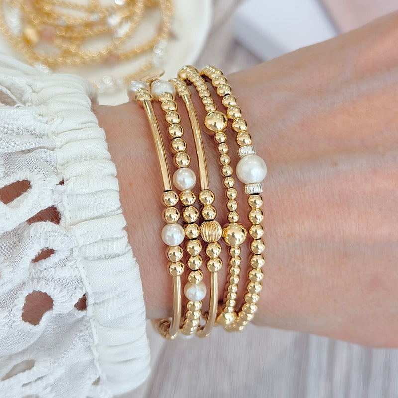 Gold beaded bracelets with pearls on a wrist against a white lace garment background