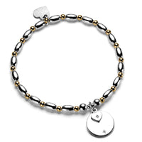 Silver and gold beaded bracelet with round disc and heart-shaped charms on a white background