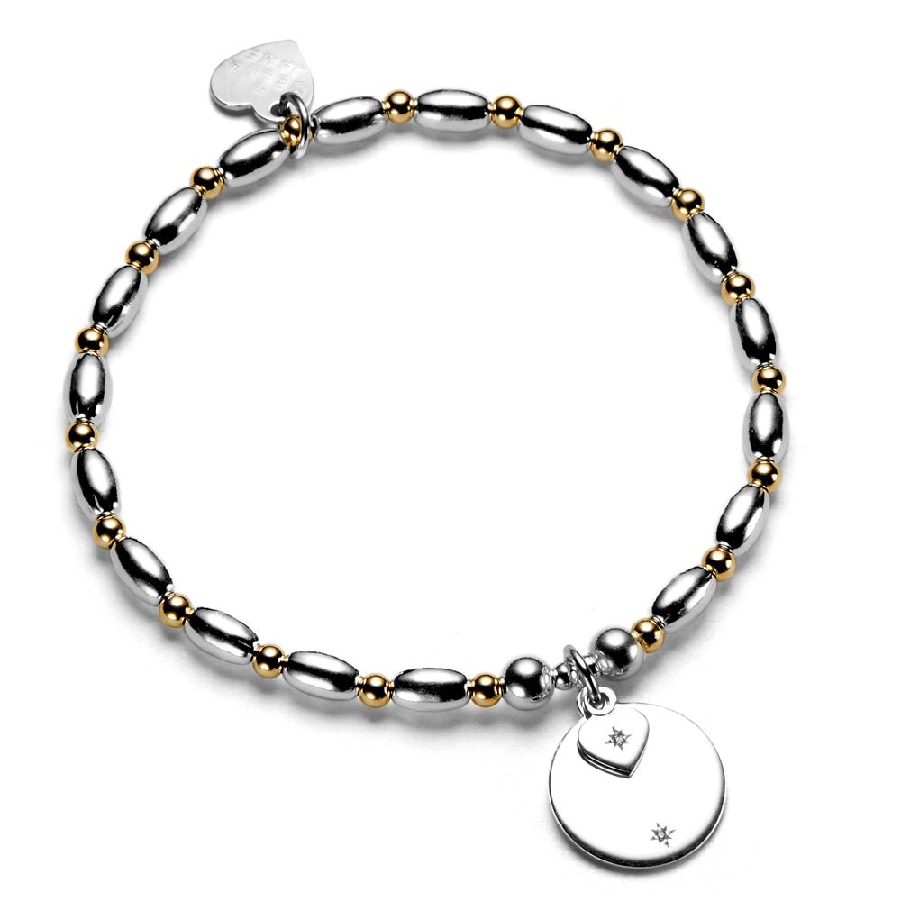 Silver and gold beaded bracelet with round disc and heart-shaped charms on a white background
