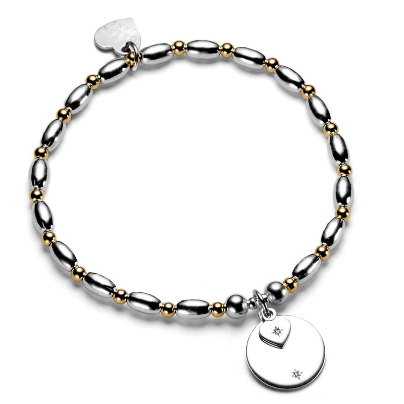 Silver and gold beaded bracelet with round disc and heart-shaped charms on a white background