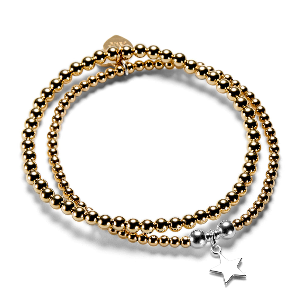 A gold-filled stacking bracelet duo with one plain gold stacking bracelet and one featuring a silver star charm, on a white background