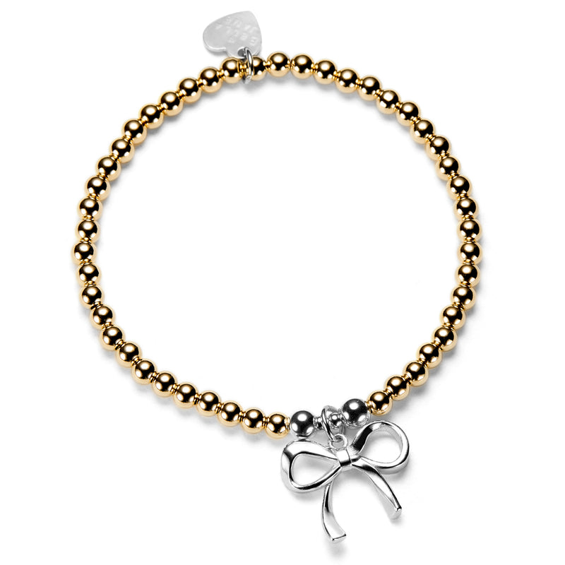 Gold beaded bracelet with a silver bow charm on a white background
