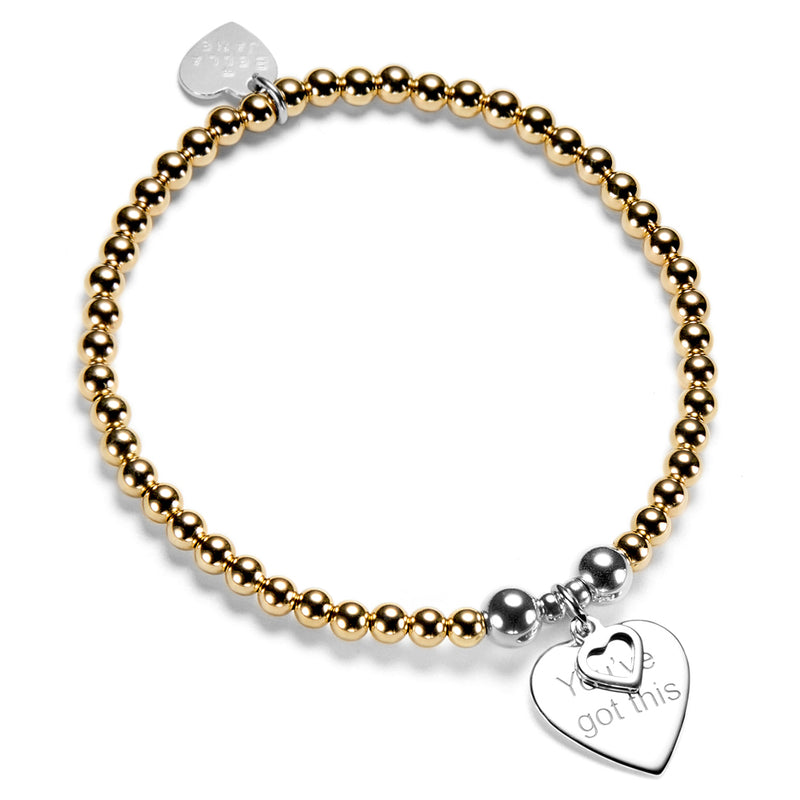 Gold beaded bracelet with silver heart charm featuring the words you've got this, on a white background