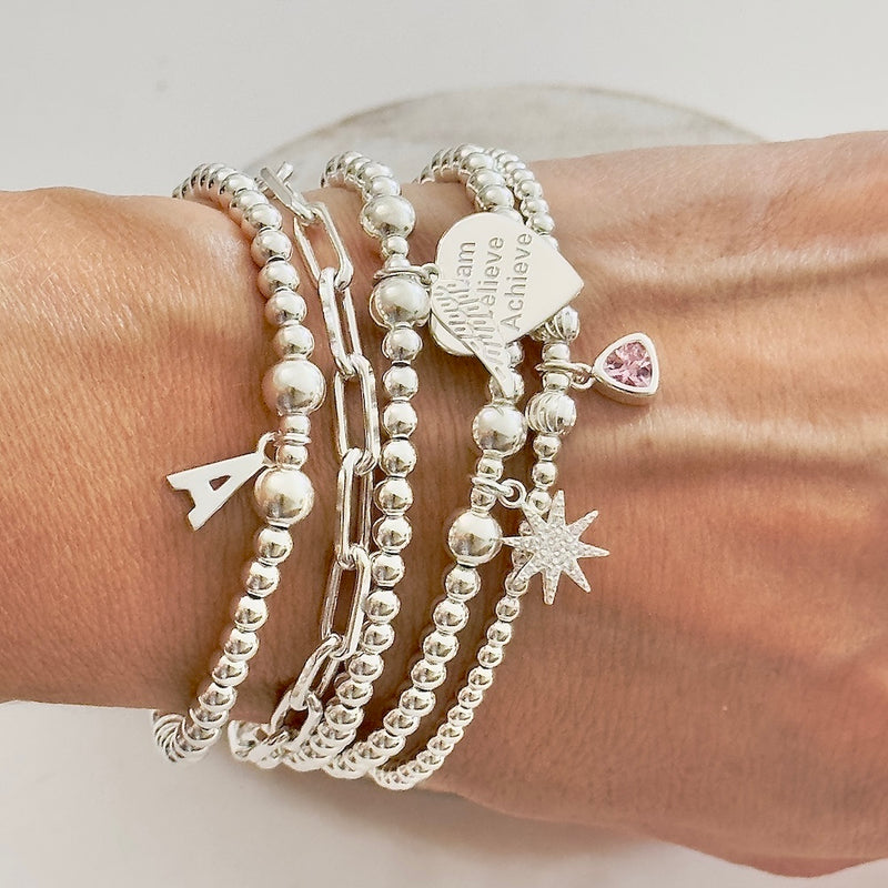 Silver bracelets with various charms on a wrist against a neutral background