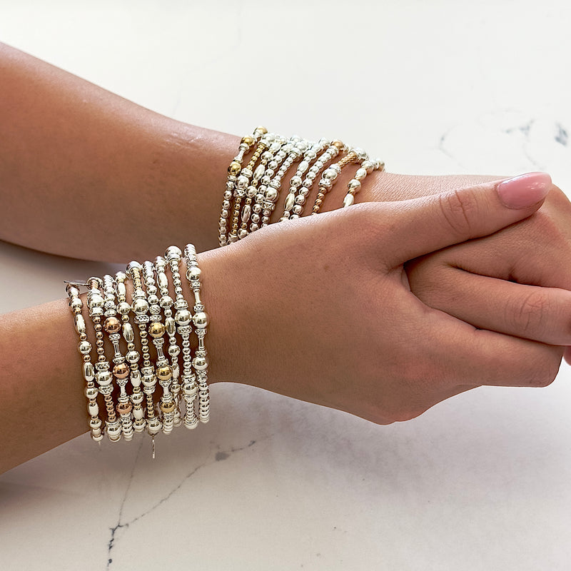 Close-up of a woman's wrists, wearing a stack of sterling silver and gold-filled beaded bracelets on each wrist.