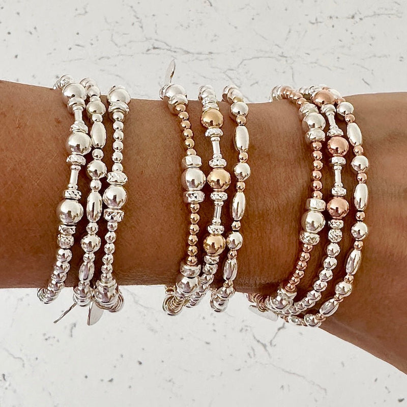 Three sets of 3 beaded bracelets in silver, gold, and rose gold on a wrist against a light background