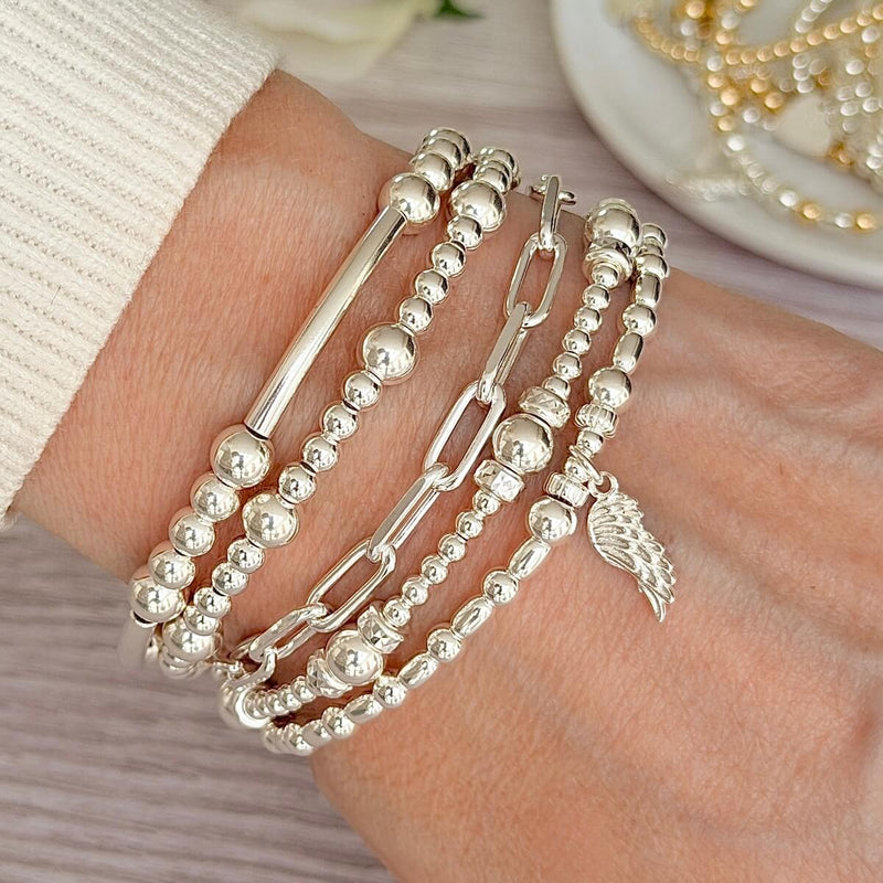 Silver beaded and chain bracelets on a wrist with a neutral background