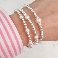 Three sterling silver and freshwater pearl beaded bracelets on a wrist with a pink and white striped shirt