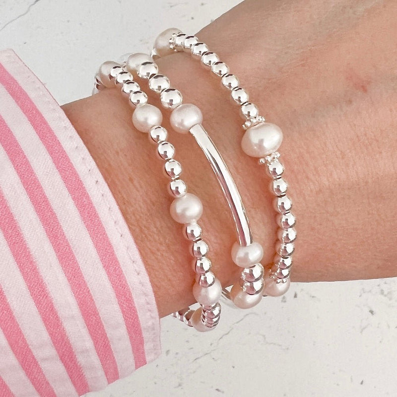 Three sterling silver and freshwater pearl beaded bracelets on a wrist with a pink and white striped shirt